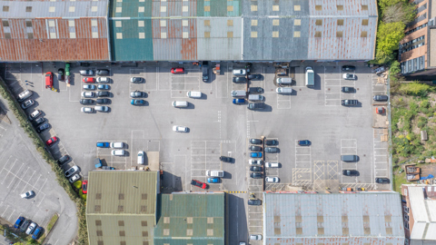 Aerial view of a large retail warehouse car park with marked parking bays and surrounding commercial buildings.