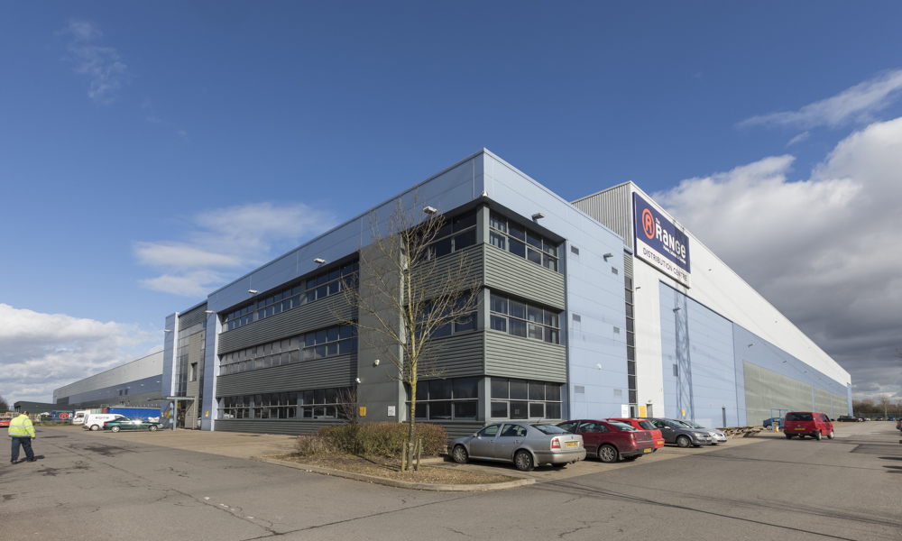 Large modern industrial warehouse with branded signage and adjacent parking area under a clear blue sky.