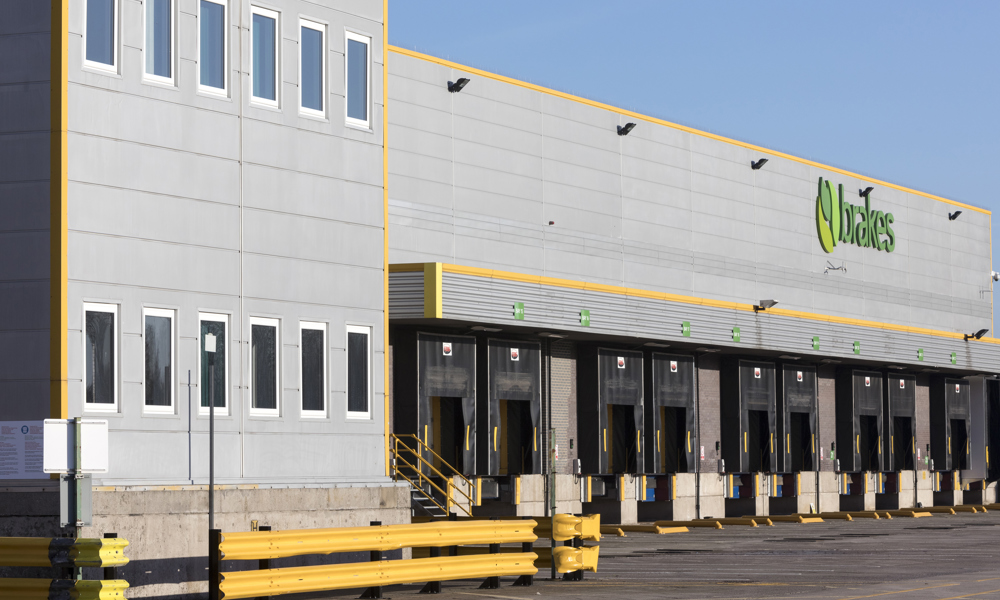 Large industrial warehouse with multiple loading docks and Brakes signage, modern UK logistics facility